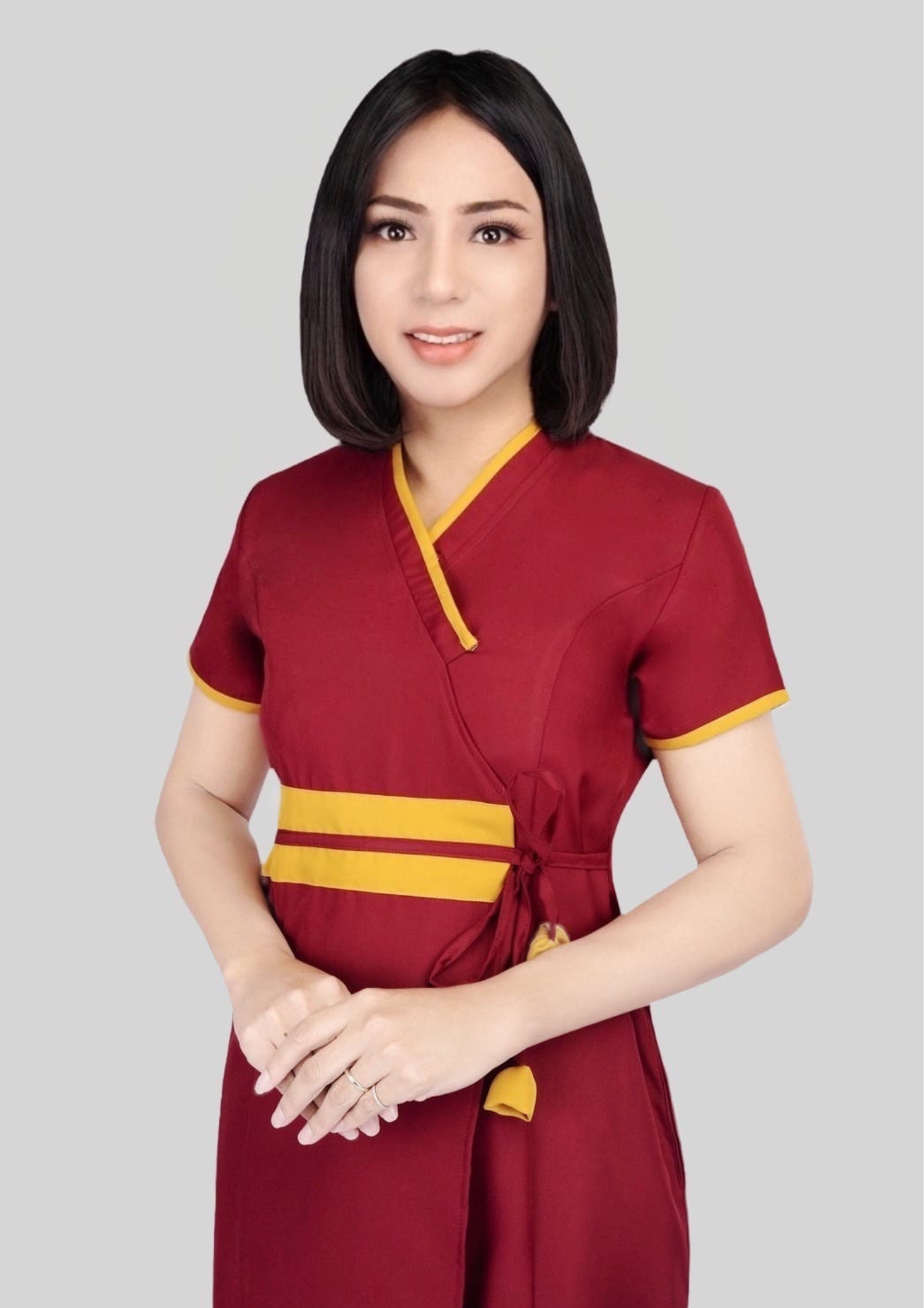A transgender massage therapist with black, shoulder-length bob haircut, wearing a red massage uniform, stood with her hands clasped in front of her.