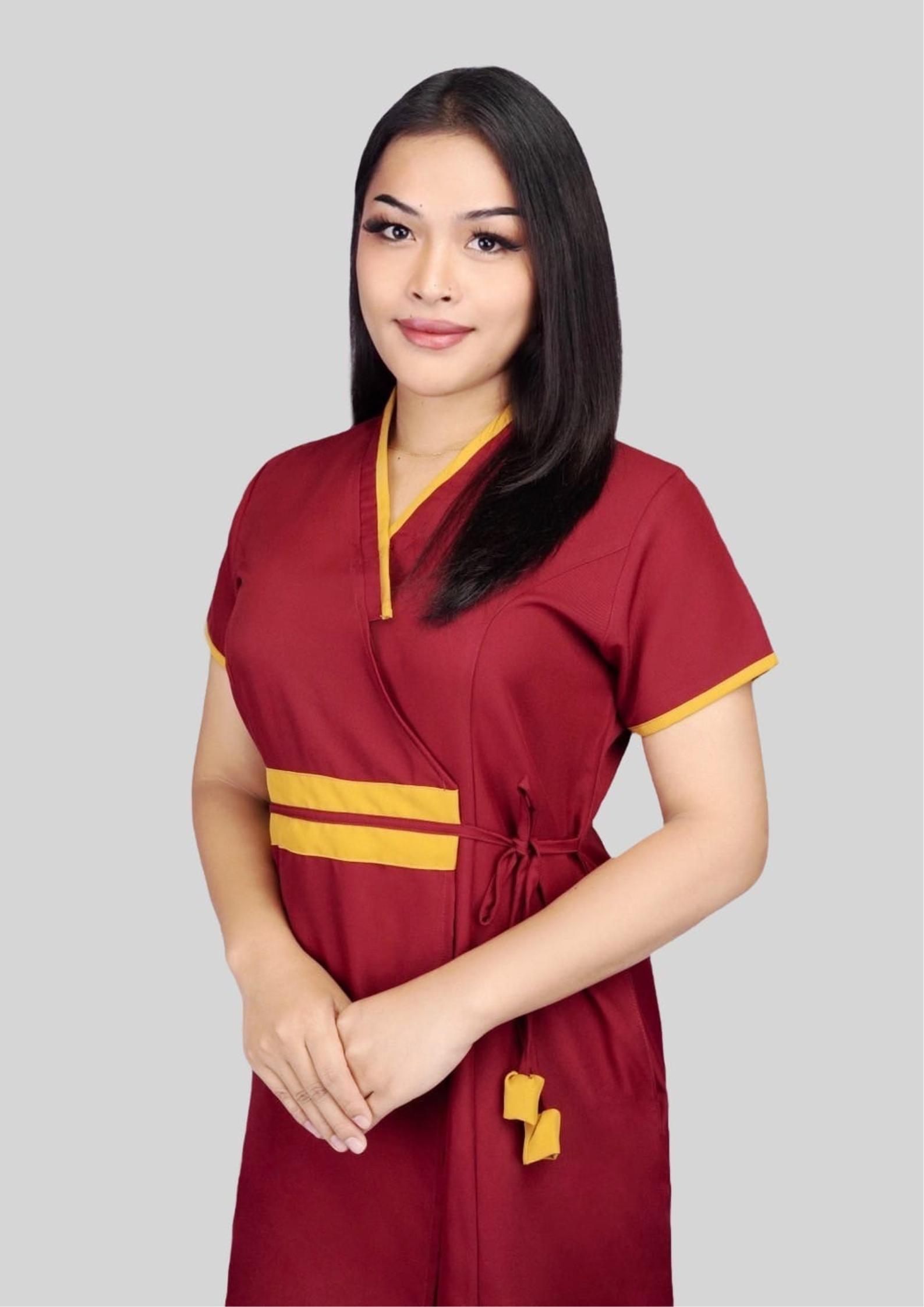 A transgender massage therapist with long, black hair, wearing a red massage uniform, stood with her hands clasped in front of her, smiling.