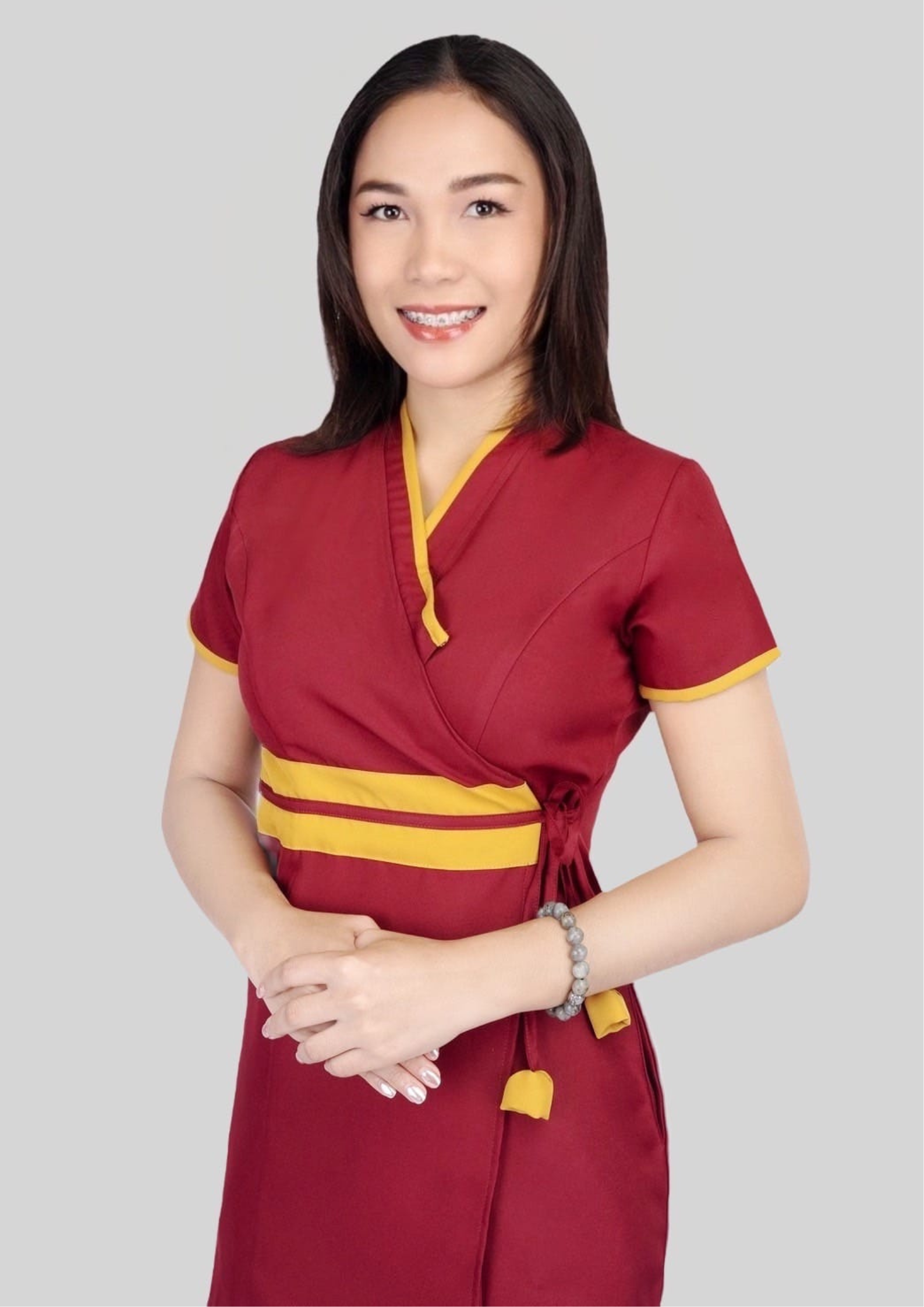 The massage therapist smiled. She had long, black hair and was wearing a red massage uniform. She stood with her hands clasped in front of her.
